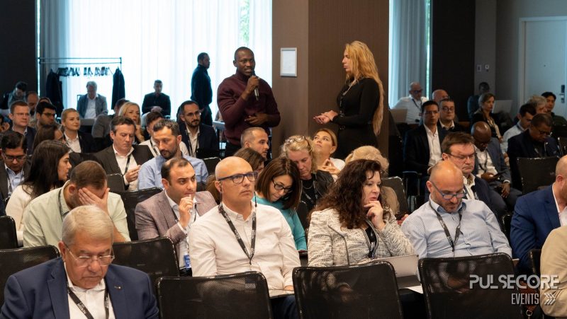 Delegates listen while an audience member stands with a microphone at a previous PulseCore event